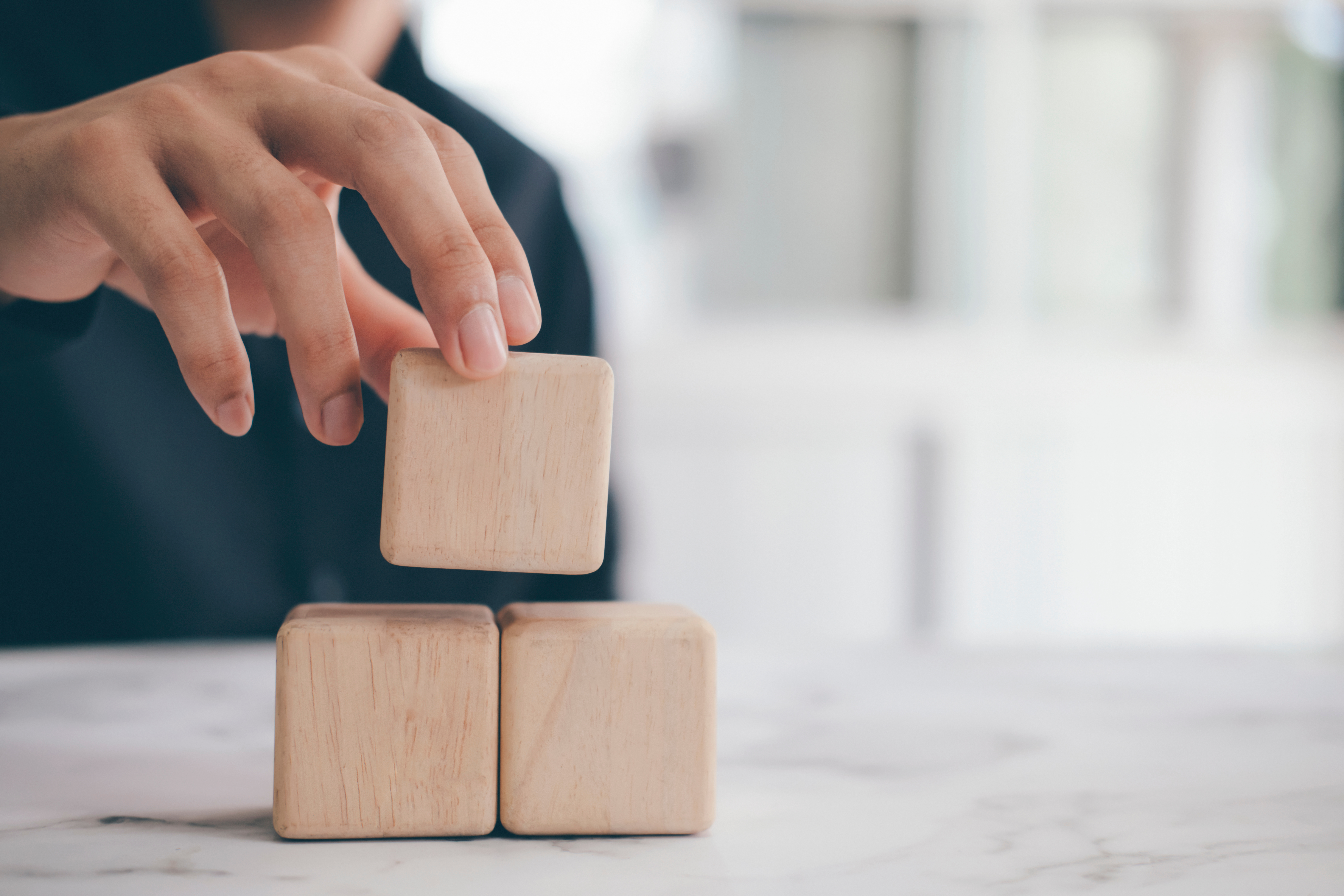 Neutral colored cube blocks being; a woman's hand is arranging them