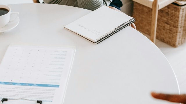 Two people seated at a table, forms, a notebook and cups of coffee are on the table. 