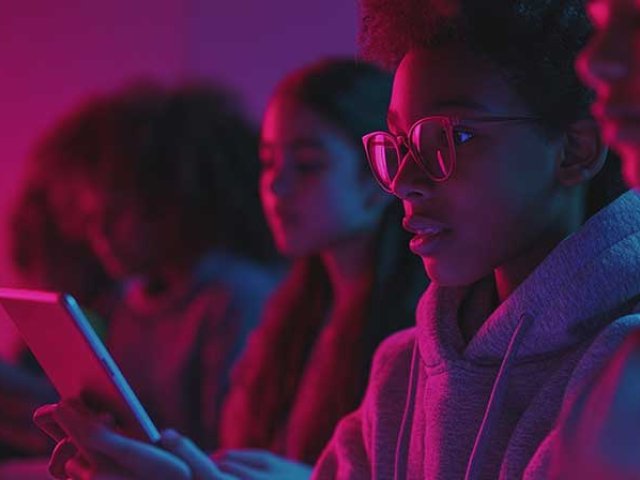 A group of teens in a vibrant pink hue light looking at mobile devices