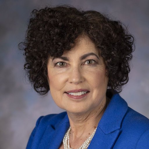 Headshot of Lynn facing the camera with a blue blazer and pearls. 